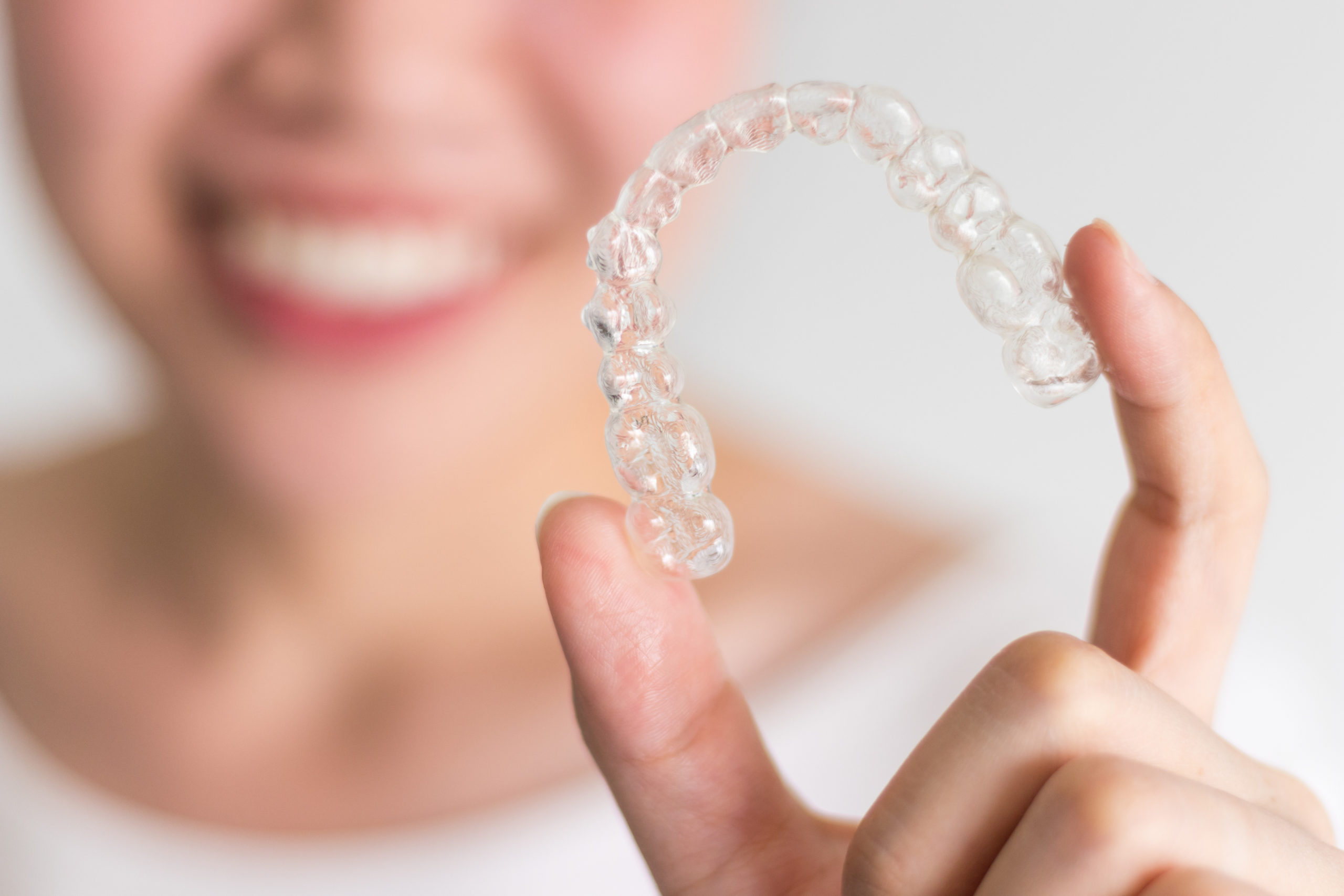 A woman holds up an Invisalign tooth aligner.